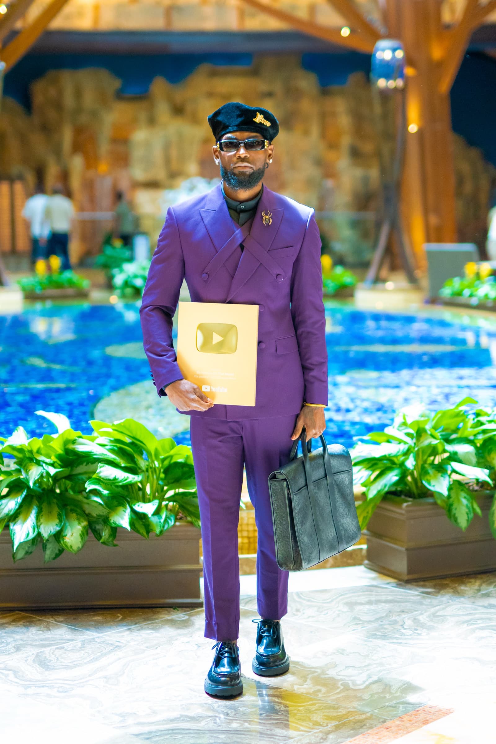 Sly Huncho in a purple suit holding a YouTube Gold Creator Award