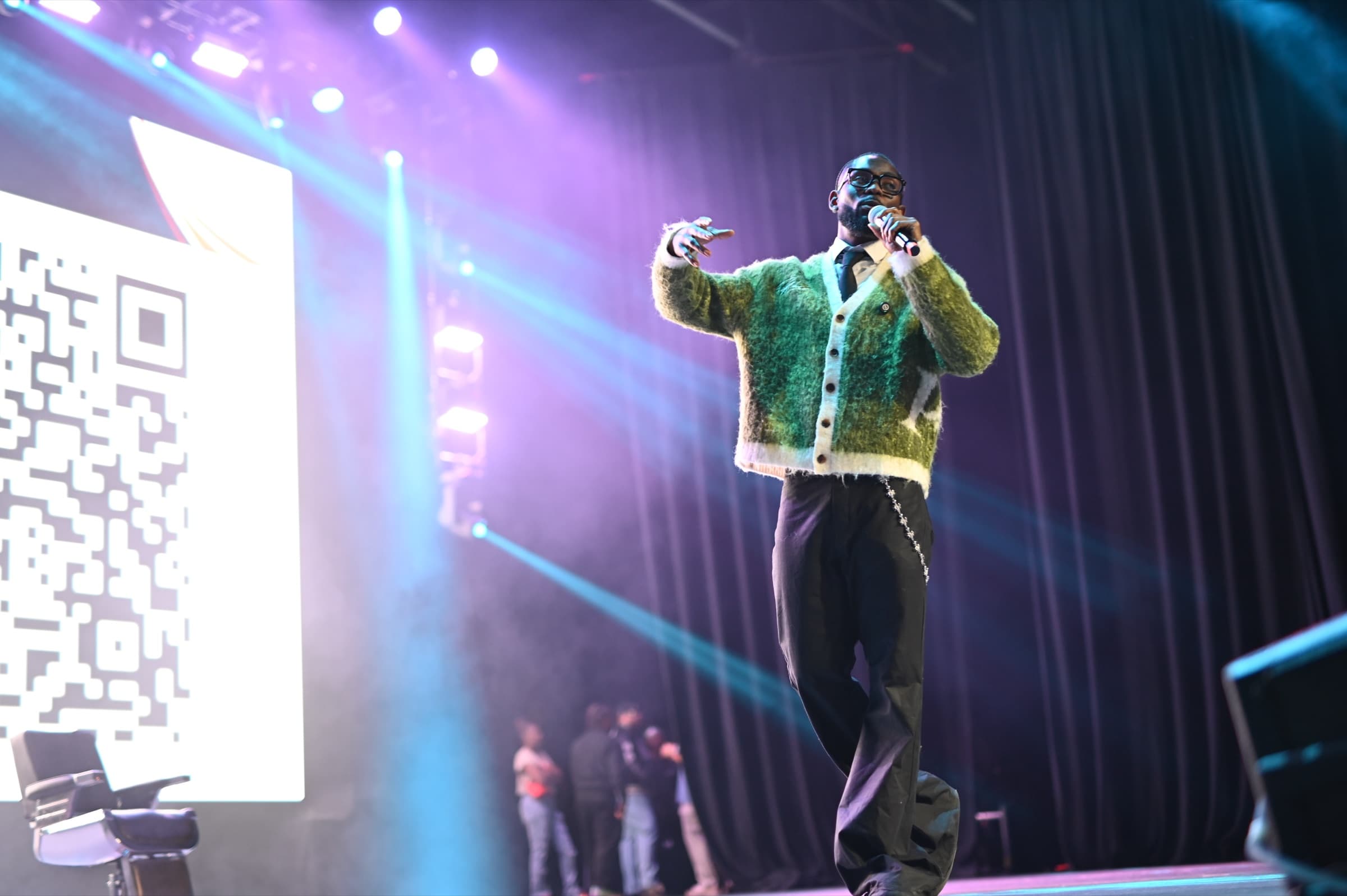 Sly Huncho speaking on stage with lights behind him
