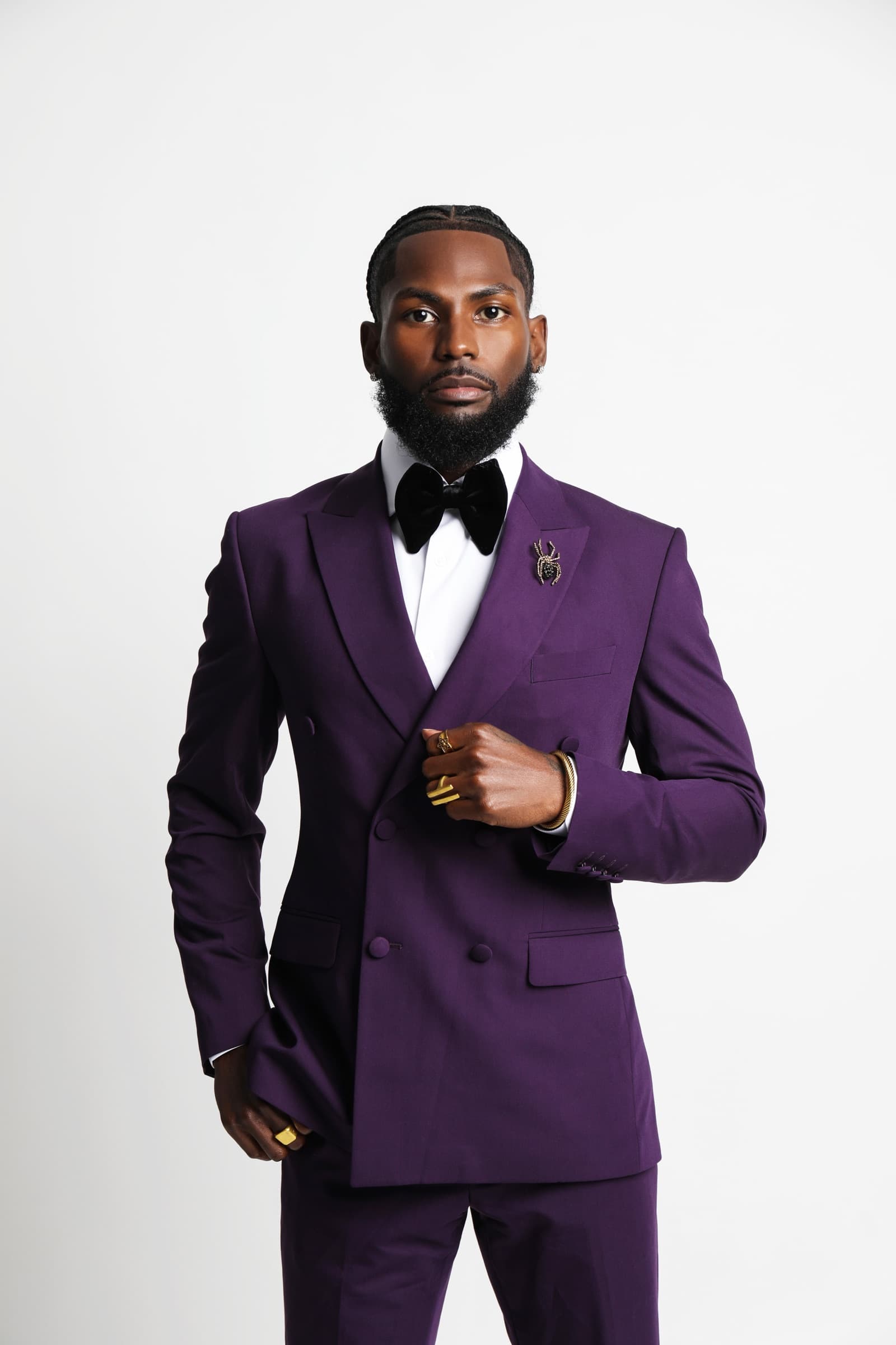 Sly Huncho standing in a purple tuxedo for a media kit portrait